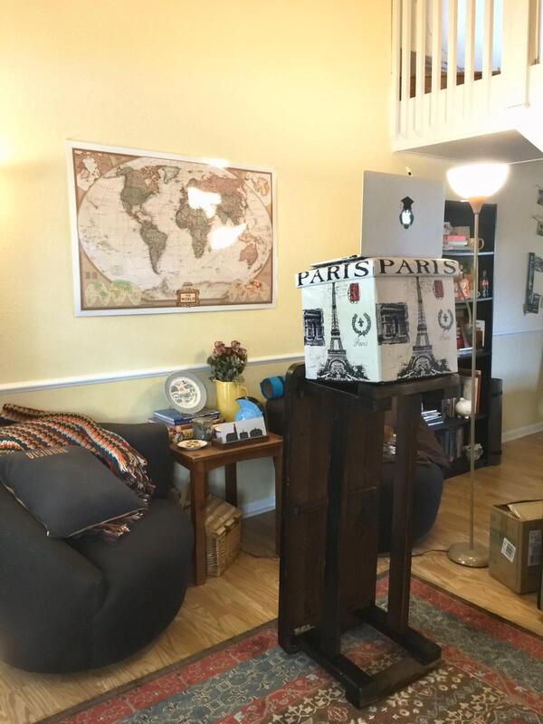 a podium made from a coffee table tipped on its side and an ottoman on top of it, carrying a laptop facing a wall with a world map
